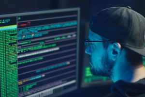 A cybersecurity expert inspecting lines of code on multiple monitors in a dimly lit office.