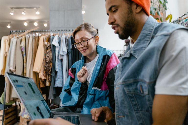 Young professionals discussing online sales strategies at a fashion store using a laptop.