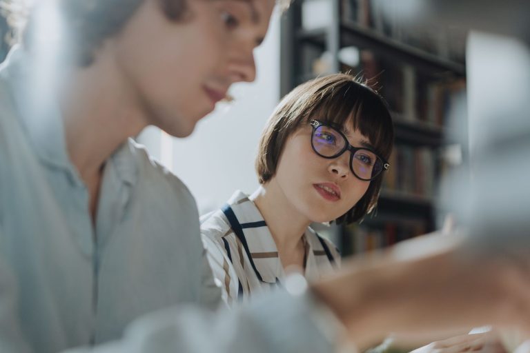 Two young adults in a library sharing ideas and discussing topics.