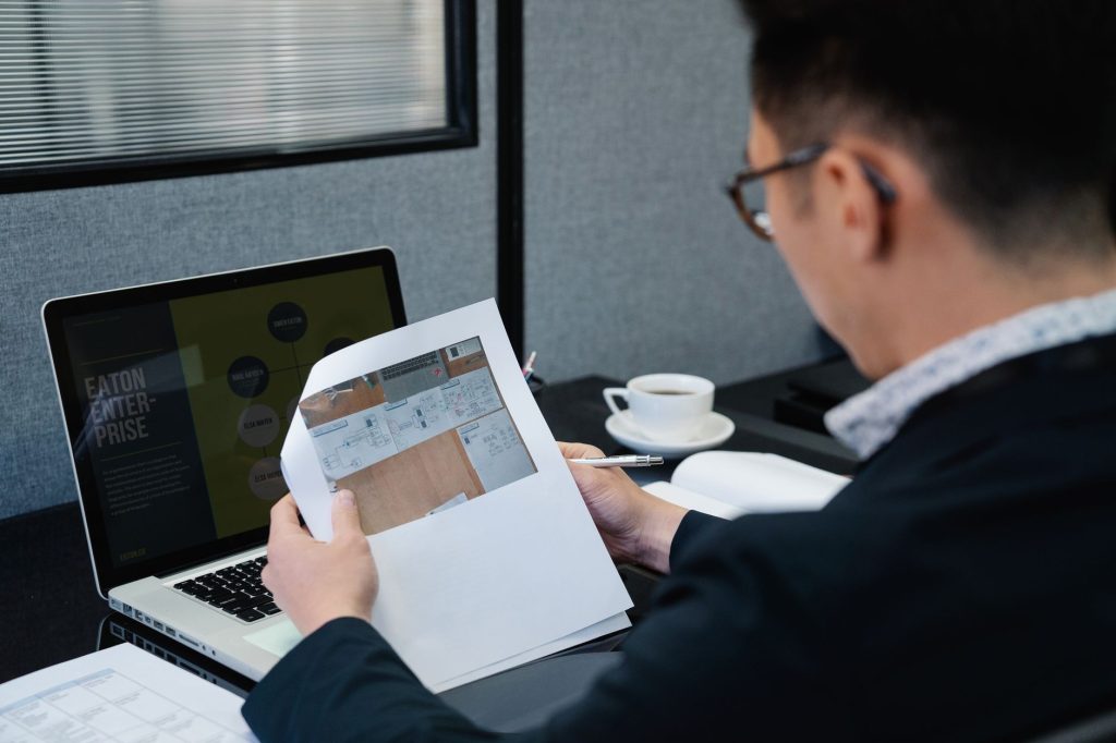 A man in an office setting analyzing documents with a laptop open nearby.